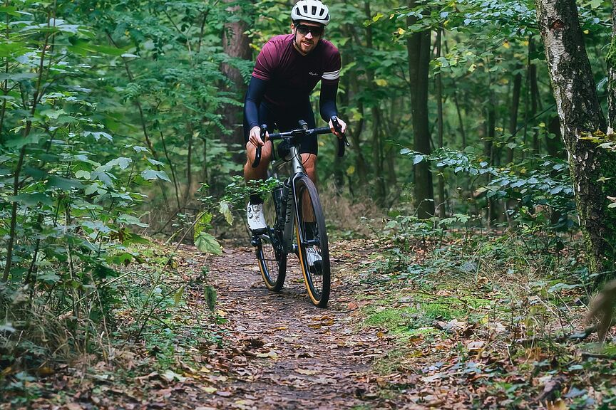 Gravelbiker im Wald Ein Gravelbiker fährt auf einem schmalen Waldpfad.